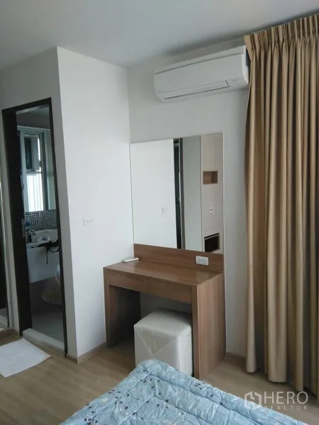 Condominium for rent or sale in Sathon, Bangkok - Bedroom vanity with mirror and stool next to bathroom door and curtains.