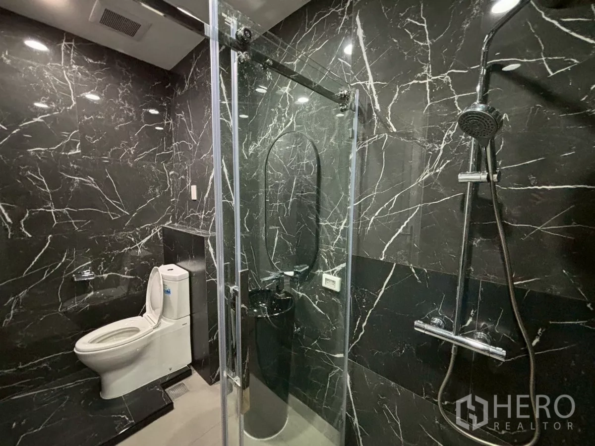 Condominium for sale in Bang Kho Laem, Bangkok - Close-up of bathroom with rain shower and sliding glass door against black marble walls.