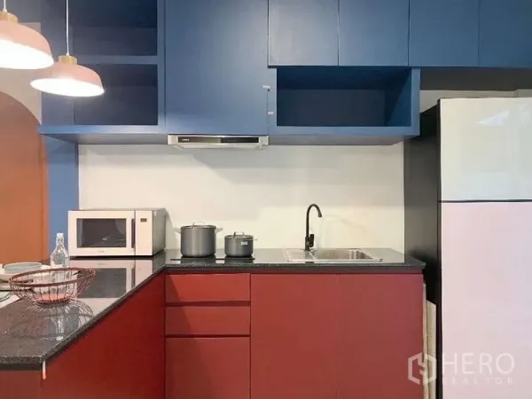 Townhouse for rent in Bang Bo, Samut Prakan - Modern L-shaped kitchen with blue upper cabinets, red base units, black granite countertop, sink and microwave.