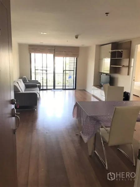 公寓 出租或出售在Watthana, Bangkok - 明亮的客餐厅，木地板、电视墙与通往阳台的落地推拉门。