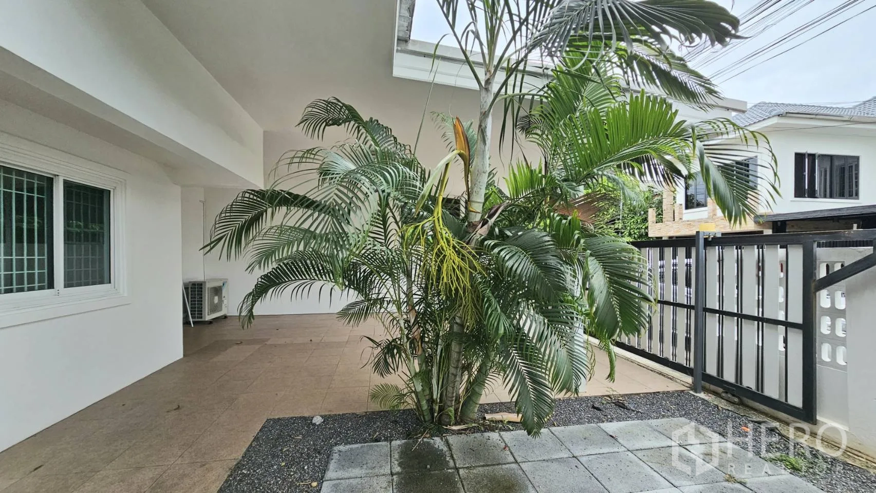 Detached House for rent in Saphan Sung, Bangkok - Covered front patio with tropical plants beside a sliding gate and tiled floor.