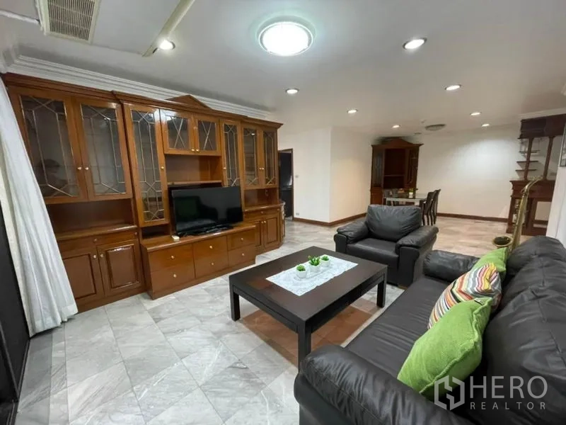 คอนโด ให้เช่าในWatthana, Bangkok - มุมนั่งเล่นอบอุ่น โซฟาหนังสีดำ ทีวี และตู้ไม้สูงเต็มผนัง