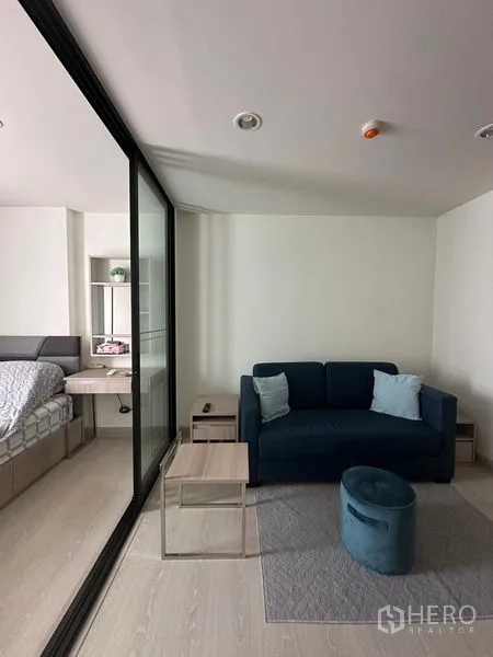 คอนโด ขายในKhlong Toei, Bangkok - ห้องนั่งเล่นมีโซฟาสีกรมท่า ข้างห้องนอนที่กั้นด้วยผนังกระจก