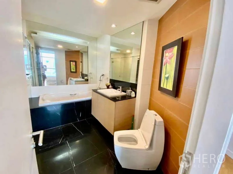 公寓 出租或出售在Sathon, Bangkok - 卫浴配浴缸、台盆与马桶，暖色点缀墙与大镜。