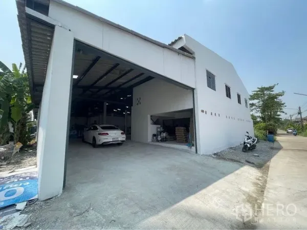 คลังสินค้า ขายในLam Luk Ka, Pathum Thani - ภายนอกโกดังสีขาว ประตูม้วนขนาดใหญ่ ทางรถเข้า พร้อมพื้นที่ลานขนถ่ายสินค้า