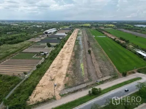 Land for sale in Sai Noi, Nonthaburi - Drone shot of wide roadside land bordered by green fields and nurseries, ideal for logistics or industrial development in Nonthaburi.