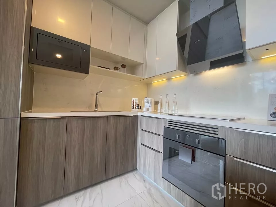 Condominium for rent in Watthana, Bangkok - Sleek kitchen with white countertops, under-cabinet lighting, microwave and ample storage.