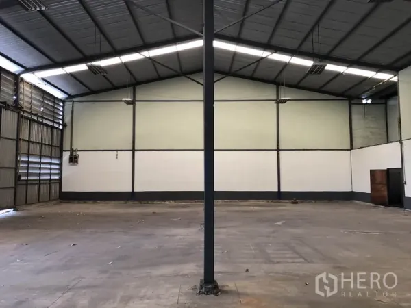 Warehouse for rent in Lam Luk Ka, Pathum Thani - Open-plan warehouse hall showing gabled roof, a central support column, and smooth concrete flooring.