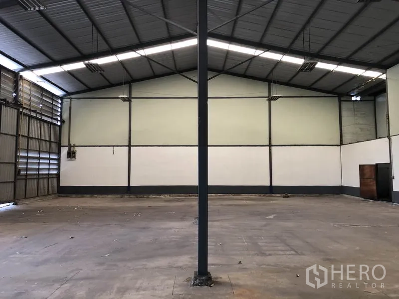 Warehouse for rent in Lam Luk Ka, Pathum Thani - Open-plan warehouse hall showing gabled roof, a central support column, and smooth concrete flooring.