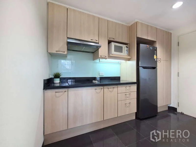 Condominium for rent in Yan Nawa, Bangkok - Full kitchen with stove hood, microwave and tall fridge in light wood finish.