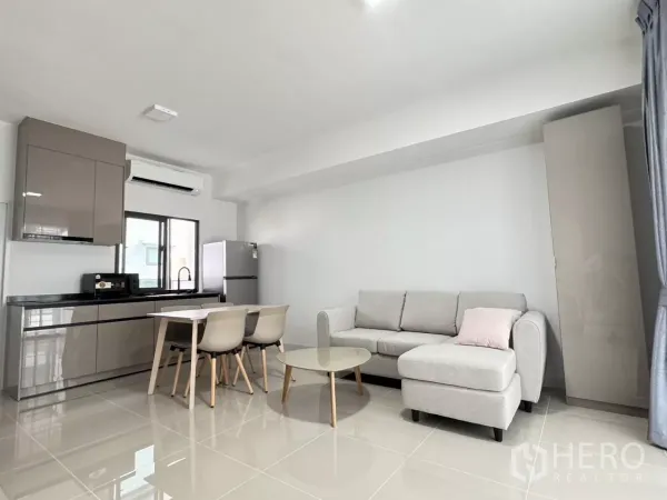 Townhouse for rent in Bang Phli, Samut Prakan - Open-plan living and dining area with sleek grey kitchen, sofa and air conditioning.