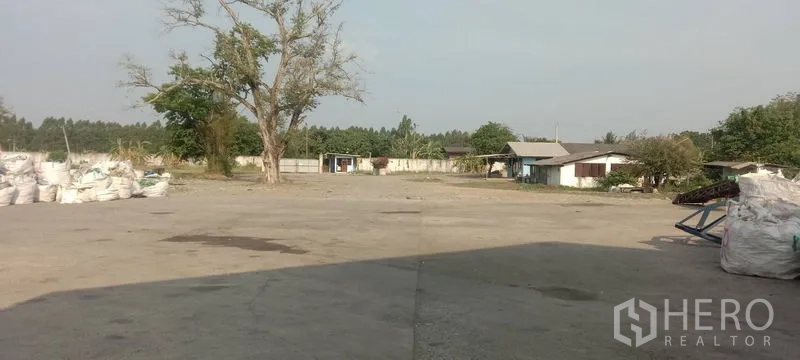 โรงงาน ขายในPhanat Nikhom, Chon Buri - ลานคอนกรีตกว้างภายในพื้นที่รั้วรอบขอบชิด มีอาคารย่อยและต้นไม้.