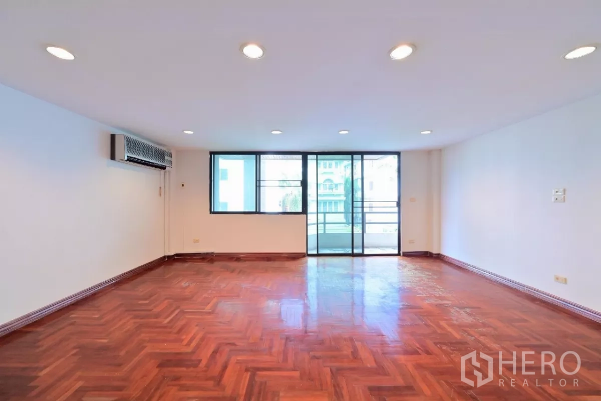 Townhouse for sale in Watthana, Bangkok - Spacious living room with parquet wood flooring, recessed lights, and balcony access.