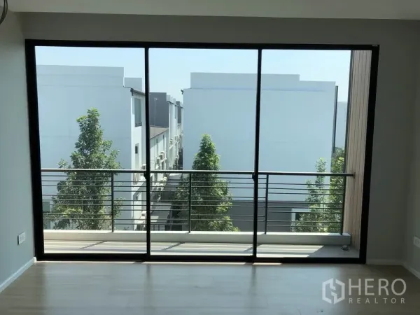 Townhouse for sale in Saphan Sung, Bangkok - Room with wide glass doors to a balcony overlooking tree-lined rows of townhouses.