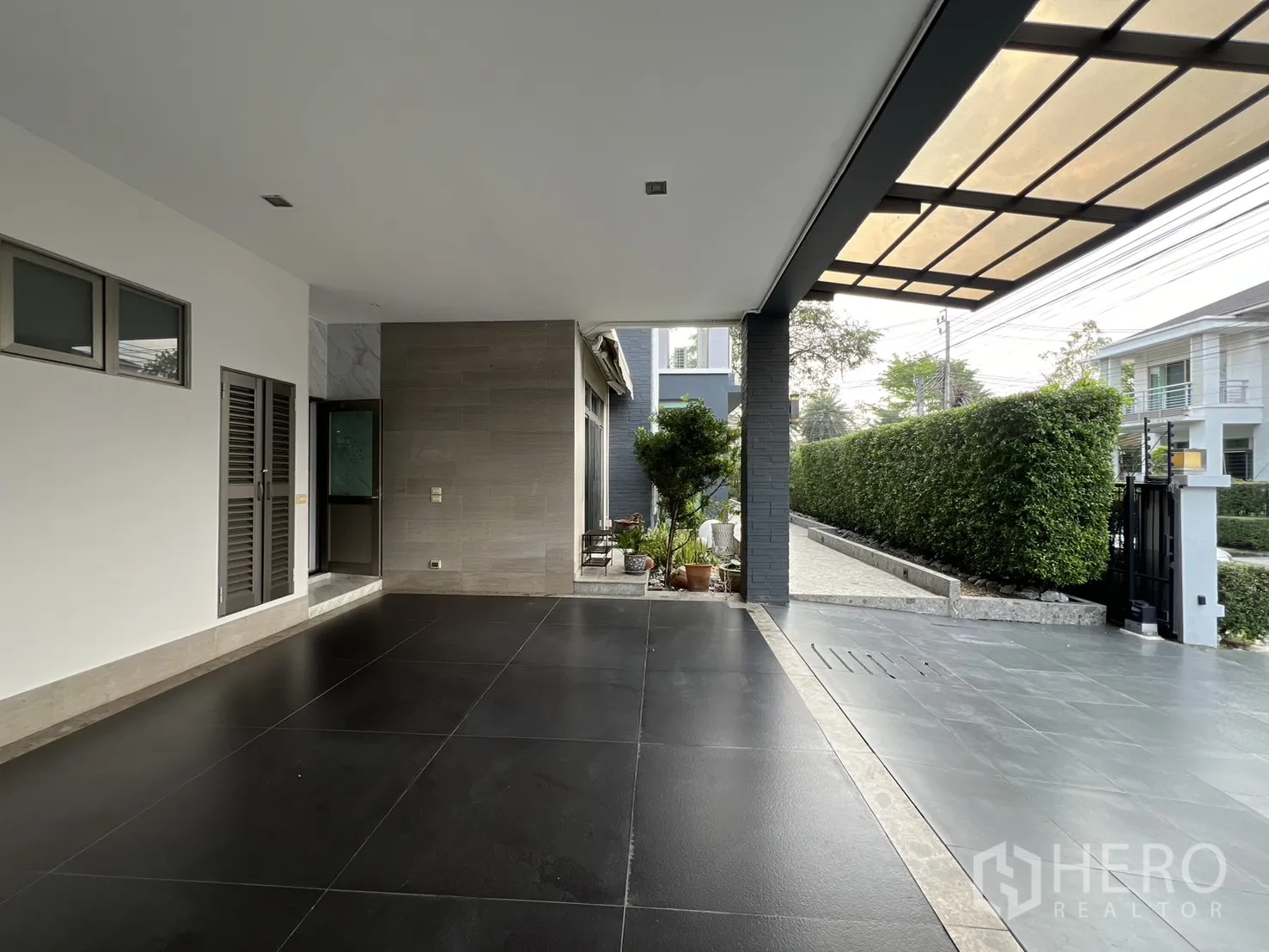 独栋房屋 for rent in Prawet, Bangkok - 带顶棚车棚，深色地砖，私密绿篱与小区大门。