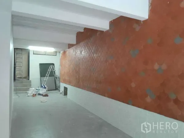 零售空间 出租在Watthana, Bangkok - 开放式店铺内景，赤陶鱼鳞纹特色墙、白色梁顶，后部台阶旁放置装修材料。