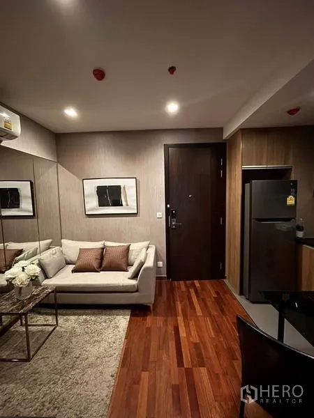 Condominium for rent or sale in Ratchathewi, Bangkok - Cozy lounge zone with light sofa, area rug, framed artwork, and refrigerator near the entrance.