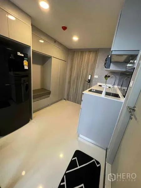 คอนโด ขายในChatuchak, Bangkok - ครัวทางเข้าพร้อมตู้บิวท์อินเต็มผนัง ตู้เย็นสีดำ และพื้นเงาสีขาว