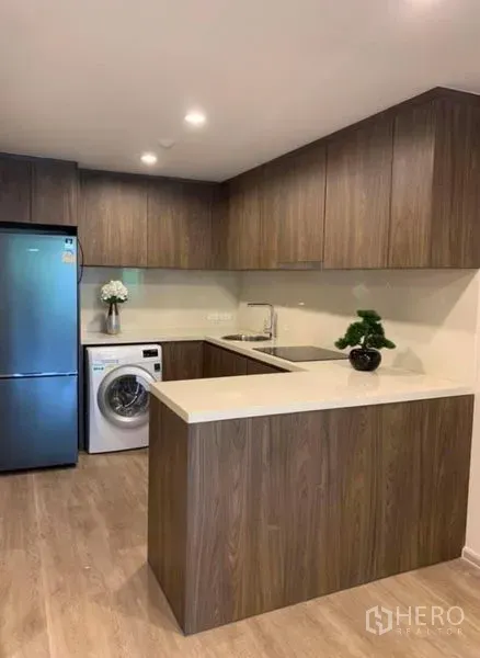 คอนโด ให้เช่าในPathum Wan, Bangkok - ครัวรูปตัว U ตู้ไม้ เคาน์เตอร์สีขาว ตู้เย็น และเครื่องซักผ้า