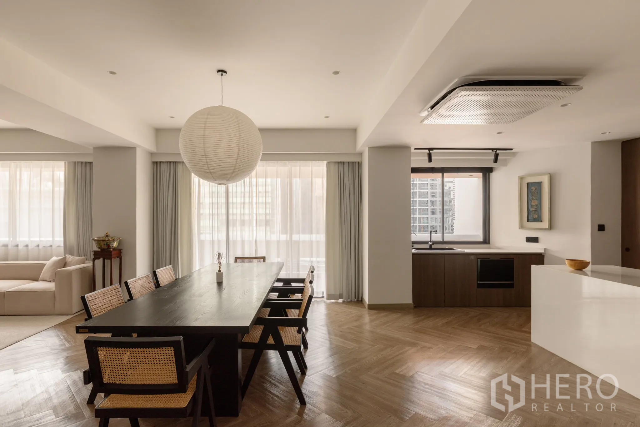 Condominium for sale in Khlong Toei, Bangkok - Open‑plan dining area with long dark table, paper pendant light, big windows and adjoining kitchen.
