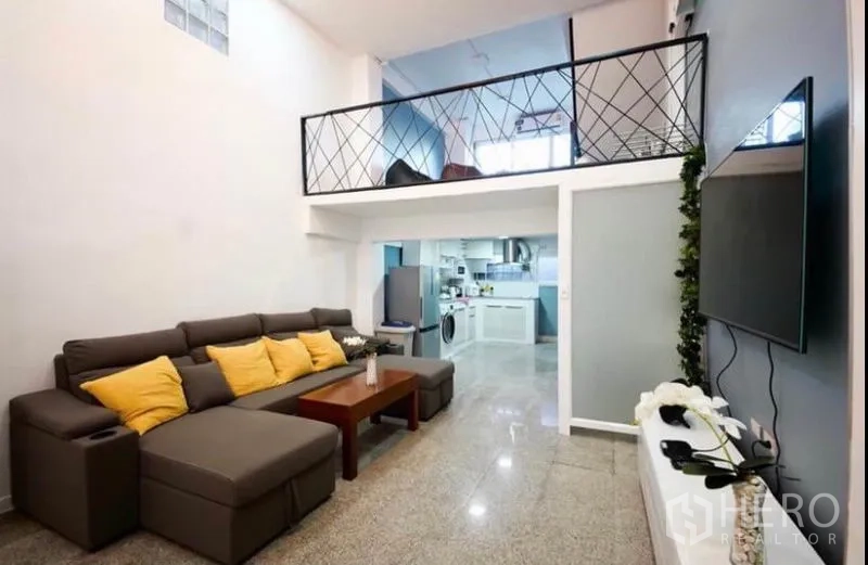 Townhouse for rent in Ratchathewi, Bangkok - Bright living room with sectional sofa, wall-mounted TV and mezzanine level above.