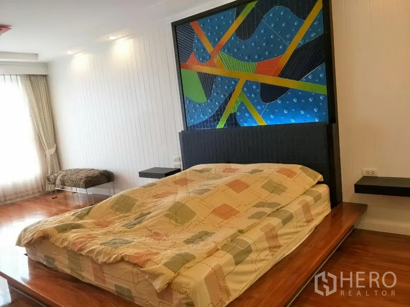 Condominium for rent or sale in Watthana, Bangkok - Spacious bedroom with colorful headboard art, platform bed and wide windows with curtains.