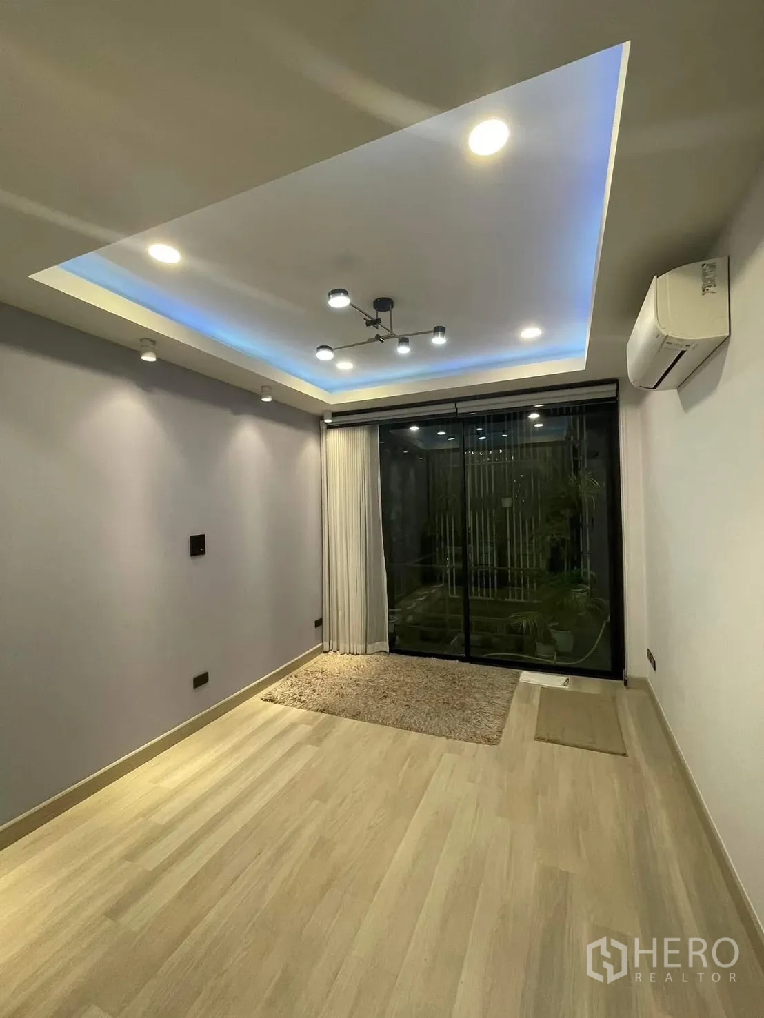 Home Office for rent or sale in Bang Kapi, Bangkok - Empty multipurpose room with cove lighting and sliding doors to a balcony garden.