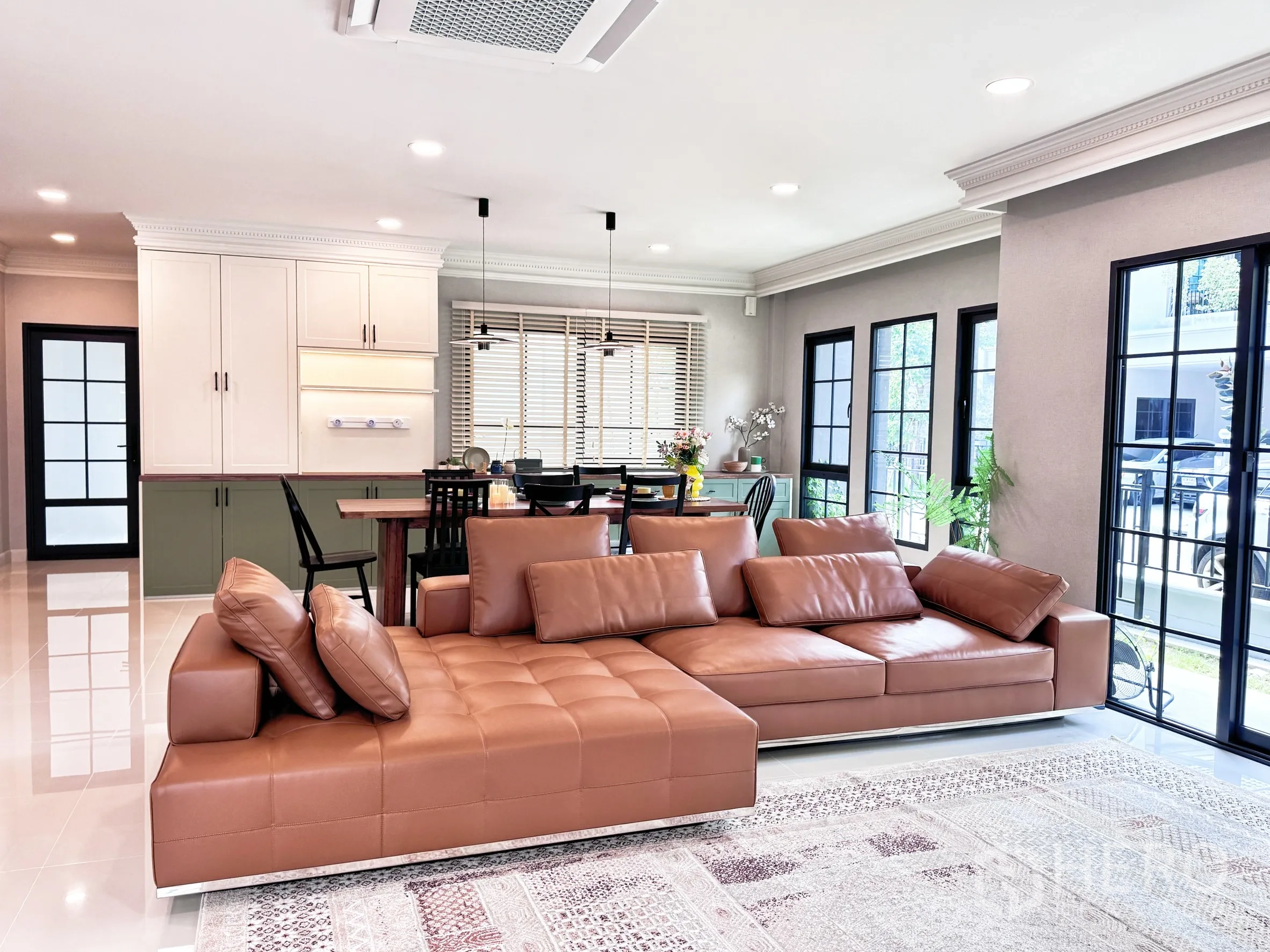 Detached House for rent in Bang Phli, Samut Prakan - Bright open-plan living room with large brown leather sectional, dining table and tall windows.