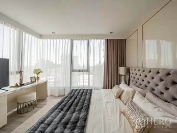 Condominium for rent in Bang Na, Bangkok - Master bedroom with tufted headboard, corner floor-to-ceiling windows and city view work desk.