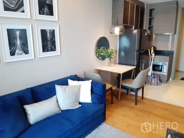 公寓 出租在Khlong Toei, Bangkok - 开放式起居区，蓝色沙发、墙面装饰与小型大理石餐角。