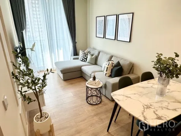 Condominium for rent in Watthana, Bangkok - Bright condo living room with L-shaped grey sofa, marble dining table and floor-to-ceiling curtains in Sukhumvit.