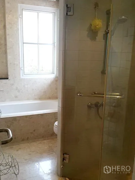 Detached House for rent in Wang Thonglang, Bangkok - Bathroom with bathtub, window and glass-enclosed shower over marble tiles.