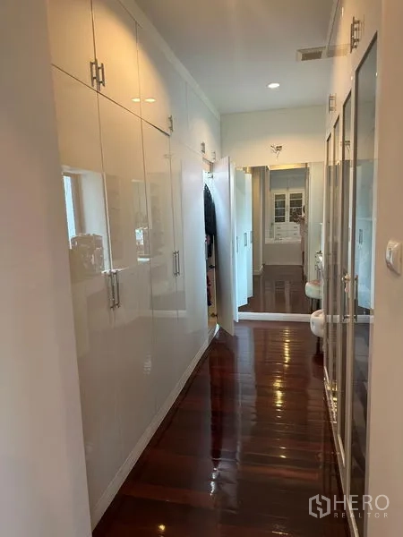 Detached House for sale in Saphan Sung, Bangkok - Bright walk-in closet with glossy white cabinetry and mirror over polished wood flooring.