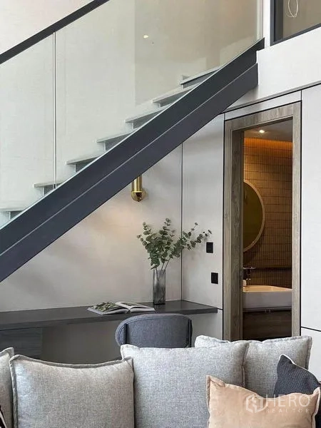 公寓 出租在Pathum Wan, Bangkok - 开放式楼梯上方设书桌，旁有通往瓷砖浴室的门，浴室配圆镜与暖色灯光。