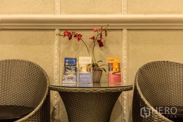 店屋 出租在Phaya Thai, Bangkok - 编织休闲椅与玻璃桌，摆放宣传册和兰花的休息角。