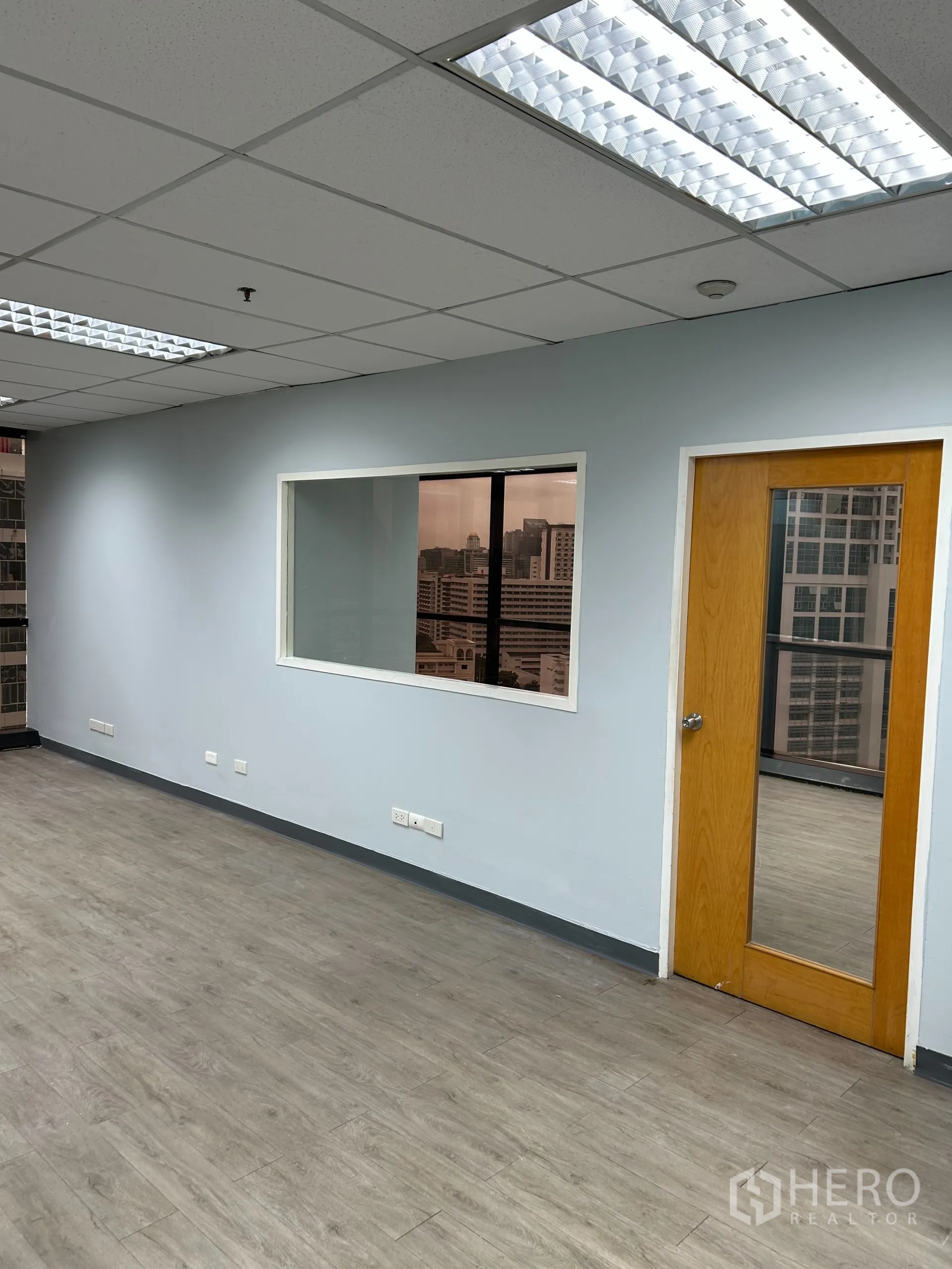 办公空间 出租在Khlong Toei, Bangkok - 内墙配透明分隔窗与木门，灰色墙面与荧光灯照明。