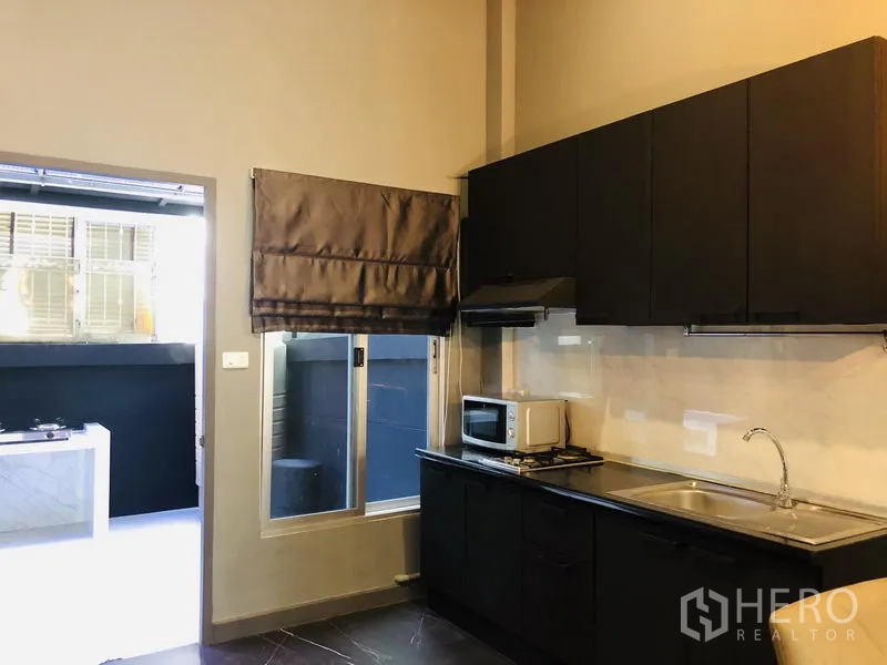 ทาวน์เฮาส์ ให้เช่าในBang Kapi, Bangkok - ครัวบิลท์อินตู้สีดำ อ่างล้างจาน เครื่องดูดควัน และหน้าต่างออกสู่ลานหลังบ้าน