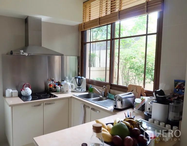 Detached House for rent in Watthana, Bangkok - Corner kitchen with large window, stainless range hood, sink, and small appliances on the counter.