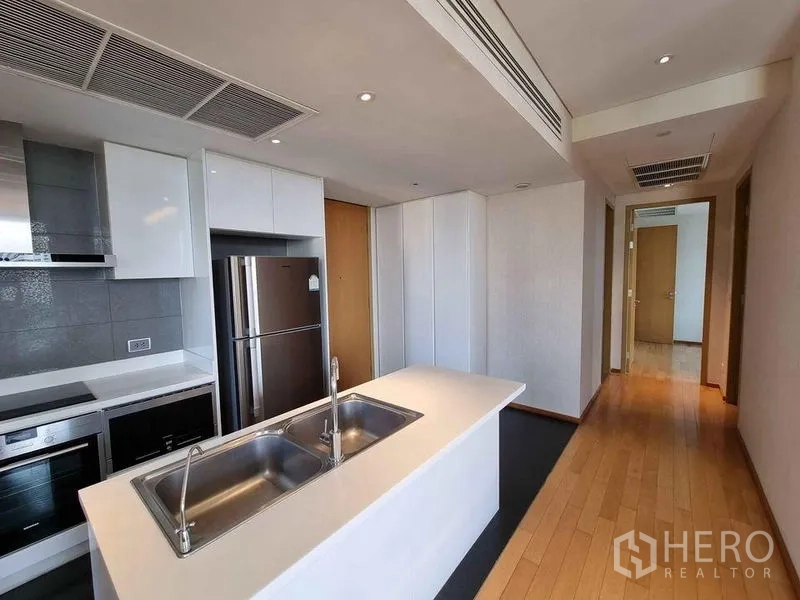 Condominium for rent in Watthana, Bangkok - Kitchen corridor featuring an island sink, built-in oven, cooktop and fridge.