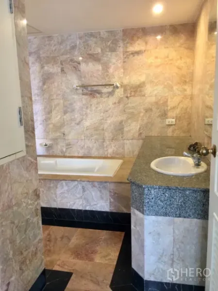 Condominium for rent or sale in Watthana, Bangkok - Marble-tiled bathroom with built-in bathtub and single vanity.