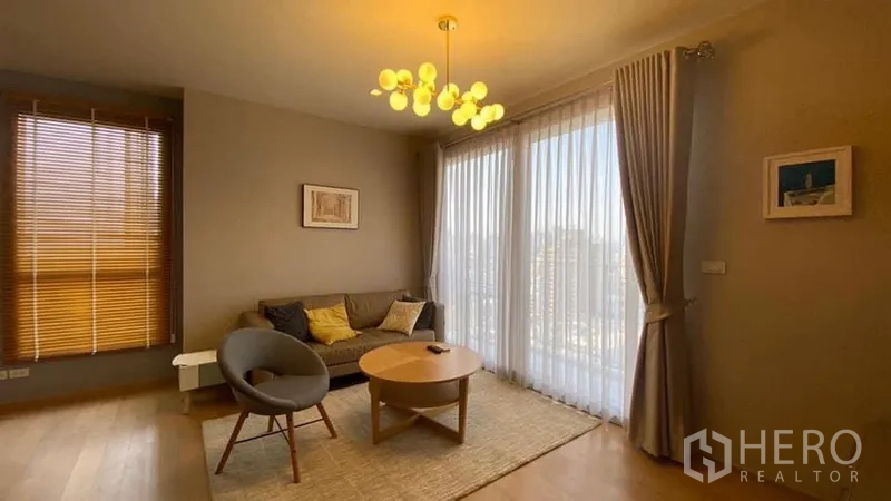 คอนโด ให้เช่าในKhlong Toei, Bangkok - ห้องนั่งเล่นอบอุ่น โซฟา โต๊ะกลางทรงกลม โคมไฟโมเดิร์น และกระจกเต็มบานมองวิวเมือง