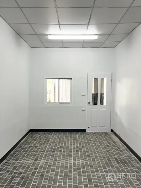 Warehouse for rent in Wang Thonglang, Bangkok - Front view of office room with window and white door over a grid-pattern tile floor.
