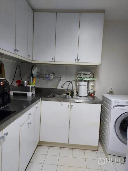 Condominium for rent or sale in Watthana, Bangkok - Compact white kitchen with upper cabinets, stainless countertop, sink and washing machine.