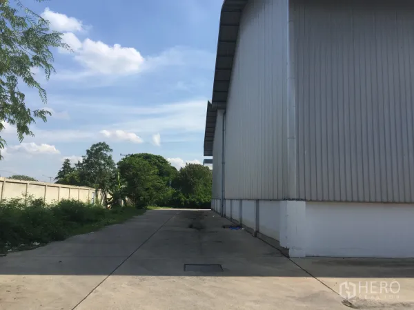 工厂 出租在Khlong Luang, Pathum Thani - 工厂侧边混凝土通道，旁有绿化与围墙。