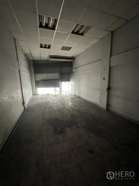 店屋 出租在Watthana, Bangkok - 一层店面进深空间，地砖、吊顶，前方卷闸门透入自然光。