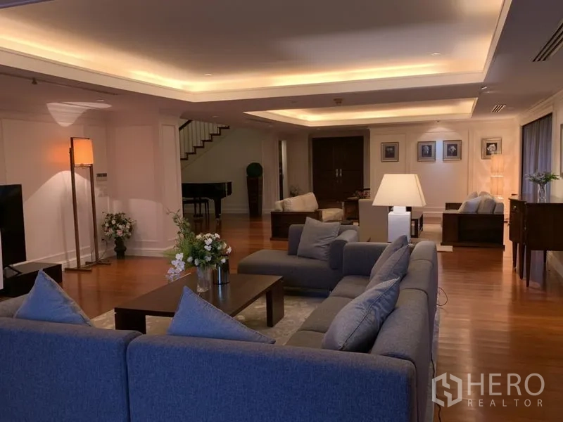 Condominium for rent or sale in Watthana, Bangkok - Spacious lounge with a gray sectional sofa, cove lighting and wooden floors.
