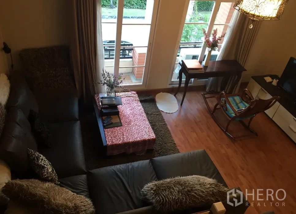 Townhouse for rent or sale in Bueng Kum, Bangkok - Upper-floor family room with large sofa, balcony doors, wood floors and TV area.