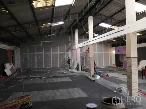 货栈 出租在Nonthaburi - 高挑仓库大厅，装修进行中，石膏板隔墙与脚手架可见。