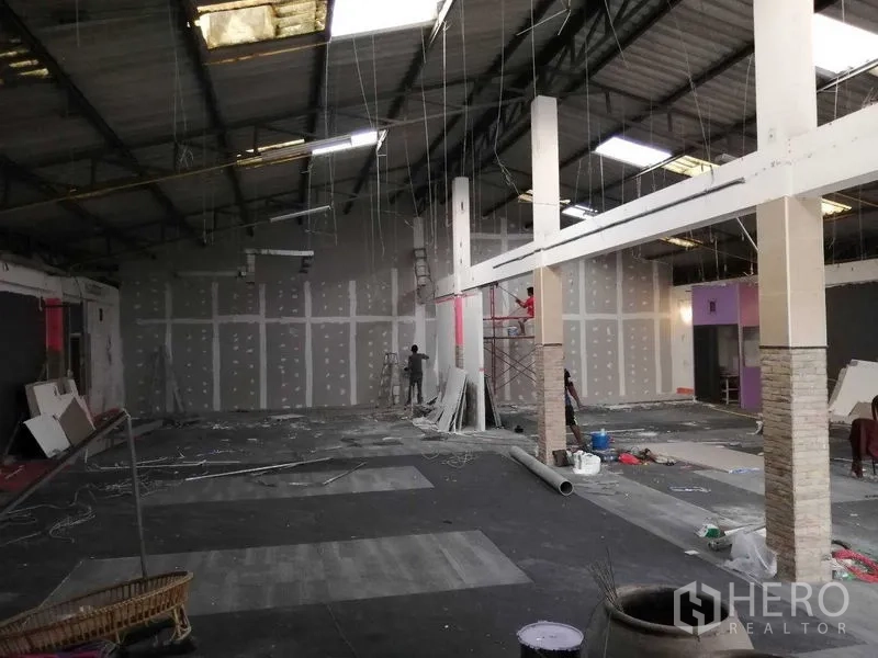 货栈 出租在Nonthaburi - 高挑仓库大厅，装修进行中，石膏板隔墙与脚手架可见。
