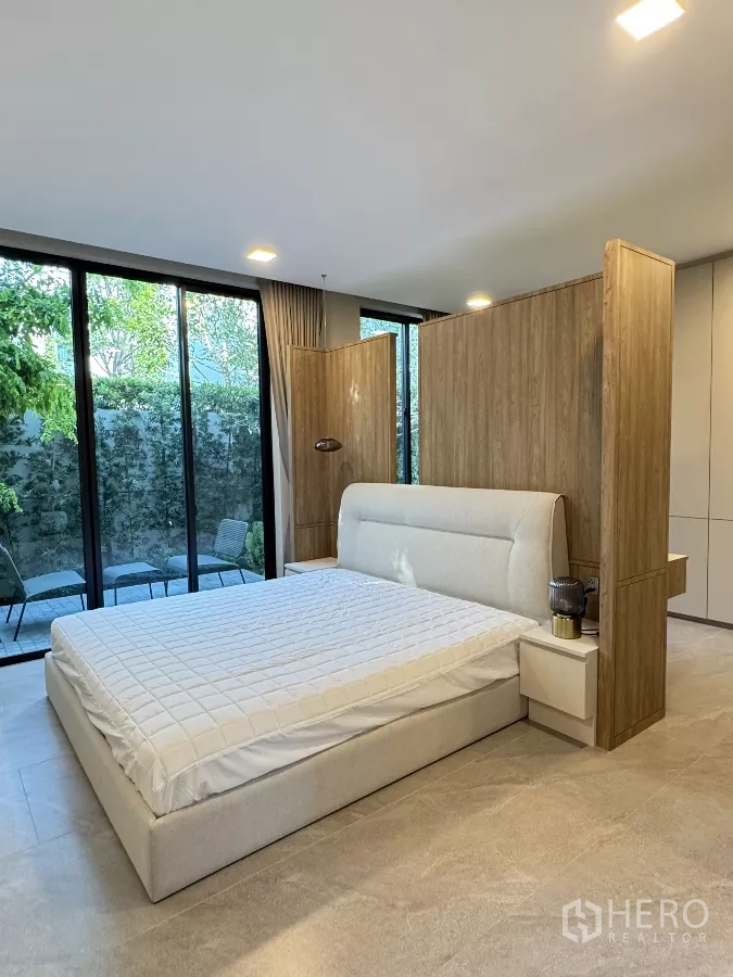 Detached House for rent in Saphan Sung, Bangkok - Ground-floor bedroom with upholstered bed, wood partition and garden access through glass doors.